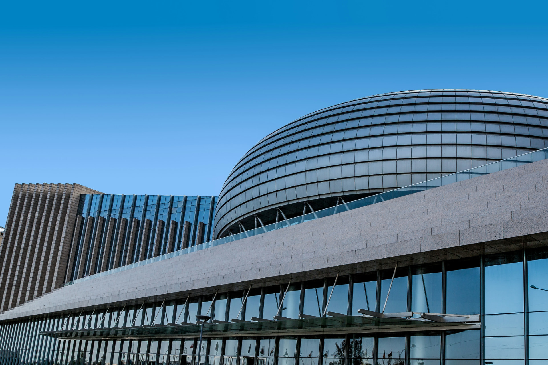 Modern civic building with a sweeping curved glass facade under a clear blue sky (stock photo)